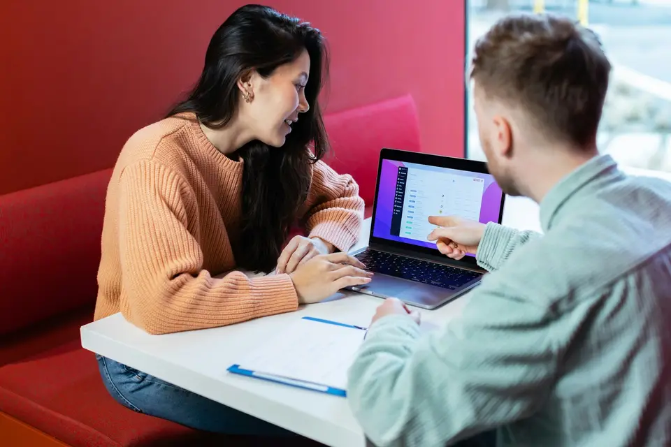 Twee collega’s bespreken hun werk aan een tafel met een laptop.