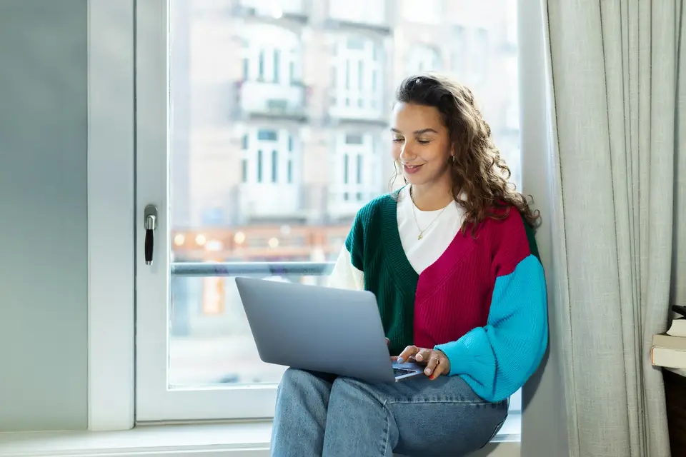 Een vrouw werkt met haar laptop bij het raam van een licht kantoor.